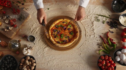 Professional chef slicing pizza by round cutter knife in restaurant kitchen.