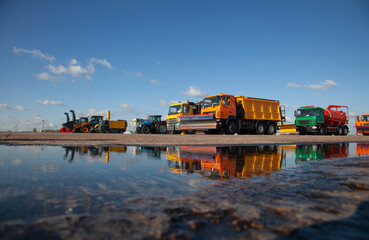 Colorful cars. Snowblower. Large snow removal machines at the airport. Road equipment. Grader, dump truck, tractor. New car reflected in a puddle. Reflection. Outdoor