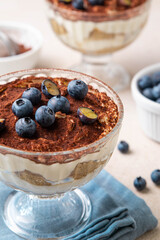 Traditional Italian dessert tiramisu with blueberries in glass. Individual homemade layered cake with berries in cup. Selective focus.