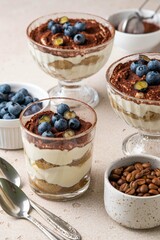 Traditional Italian dessert tiramisu with blueberries in glass. Individual homemade layered cake with berries in cup. Selective focus.