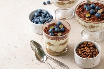 Traditional Italian dessert tiramisu with blueberries in glass. Individual homemade layered cake with berries in cup. Selective focus.