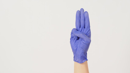 A hand sign of 3 fingers points upward meaning three, third, or used in protest. Handwear violet  latex glove. It is put on white background