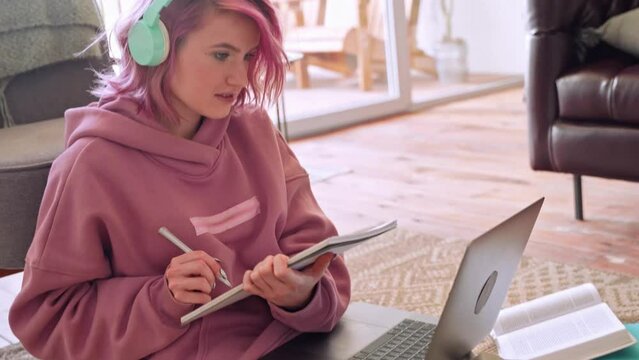 Teen girl college student with pink hair learning online on laptop computer sitting on floor at home.