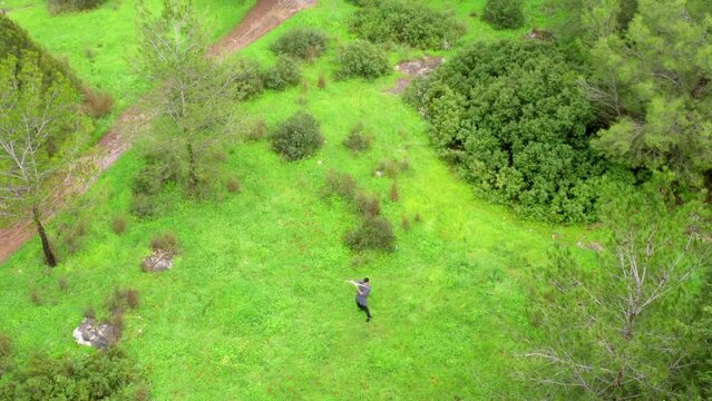 Aerial Tilt Up Shot Of Flutist Playing Flute On Green Landscape In National Forest - Ben Shemen Forest, Israel
