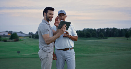 Wealthy men video call tablet device on golf course. Friends talk online outside
