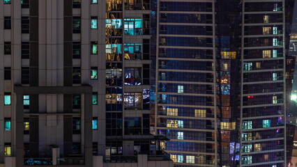 Fototapeta na wymiar Apartment windows of a glazed skyscraper glow at night with city lights reflection aerial timelapse.