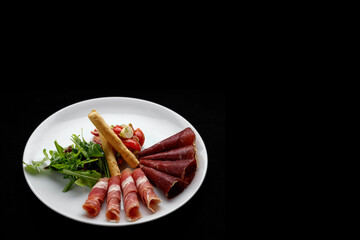 Meat appetizer with vegetable salad, arugula and grissini. Antipasti