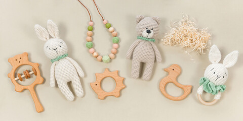 Fototapeta na wymiar Infant toys on a pastel beige background. Wooden and crocketed baby handmade toys for a banner in eco style. Baby toys concept. Wooden rattles, knitted teddy bear and teething beads top view.