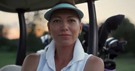 Smiling golf player relax sitting at golf cart buggy on summer sunset course.