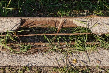 a piece of an old broken concrete pillar with rusty brown iron bars lies in the green grass on the street