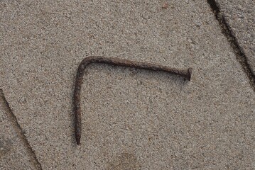 one old brown rusty bent iron nail lies on a gray stone pavement in the street