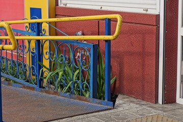 blue yellow metal handrails with a rusty railroad track near the red concrete wall of the building on the street in green grass