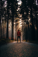 adventurous traveller stands on a dirt road at sunset in a spruce forest and watches the rays of the sun passing through the darkness of the forest. Real people and their ambitions