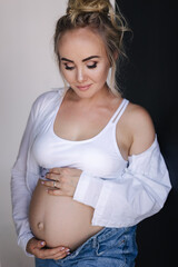 Portrait of pregnant woman in studio. Denim style. Beautiful future mother put her her hands on her belly