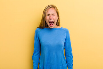young adult blonde pretty woman shouting aggressively, looking very angry, frustrated, outraged or...