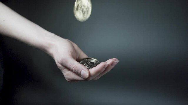 Hand catching falling golden cryptocurrency coins, black background.