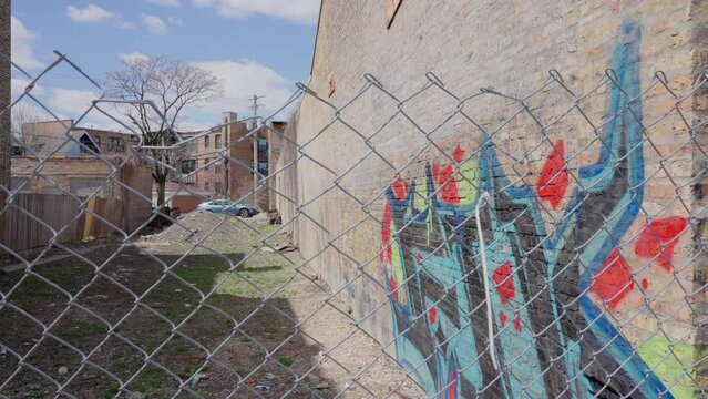 Graffiti on brick wall bordering empty lot behind chain link fence in bad neighborhood