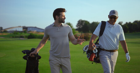 Successful golfers smiling discuss golf on course. Two men enjoy sport action.