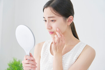 リビングでハンドミラーで顔を見て困っている女性