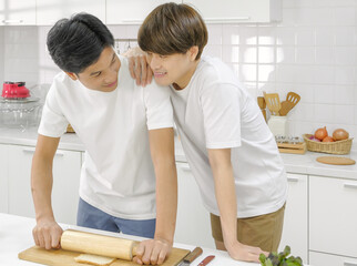 Young asian male LGBT couple happy looking eye contact together during cooking bread salad in white...