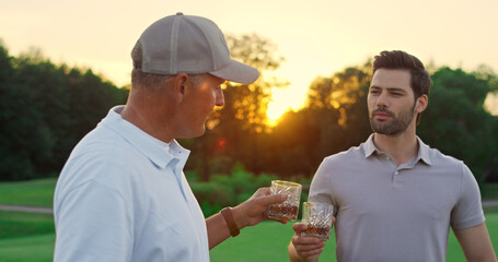 Two golfers chatting together at green course. Golf team drink whiskey outside.