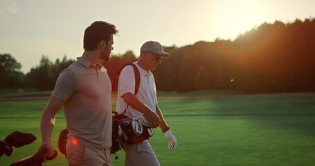 Businessmen walking golf course outside. Two players carry clubs in sportswear.