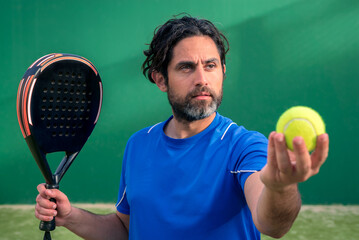 Monitor of padel holding black racket with yellow tennis ball in the hand.