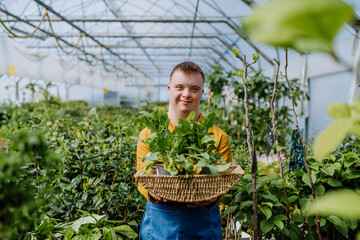 Young man with Down syndrome working in garden centre, carrying basket with plants.