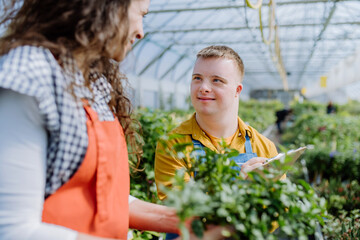 Experienced woman florist helping young employee with Down syndrome in garden centre.