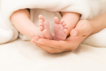 Obraz na płótnie Canvas Young adult mother hand holding and showing newborn cute small bare feet on white soft blanket in bed. Lovely emotional, sentimental moment. Closeup. Parent love. Front view.