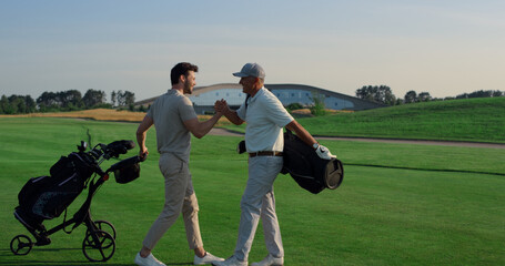 Golf players shaking hands on grass field. Two friends meeting play on weekend.