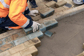 a worker in a protective work suit lays paving slabs. A professional