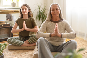 Grandmother with granddaughter sitting on floor and meditating at home