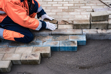 a worker in a protective work suit lays paving slabs. A professional