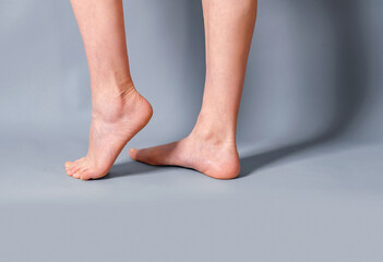 Female long bare legs on a gray background. Feet standing on toes. Spurs on the heels. Beauty salon, depilation, care, medicine, varicose veins, cosmetic surgery, spa.