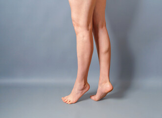 Female long bare legs on a gray background. Feet standing on toes. Spurs on the heels. Beauty...