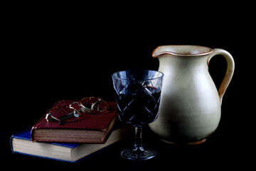 Old Books with Wine Jug and Glass of Wine and Spectacles on a Black Cloth Surface