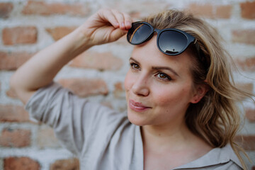 Fashion portrait of young woman with sunglasses in summer on brick wall background