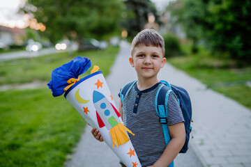 Little kid boy with school satchel on first day of school, holding school cone with gifts - obrazy, fototapety, plakaty