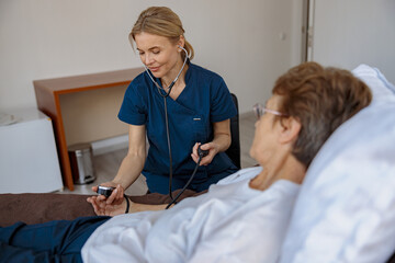 Female nurse checking blood pressure of senior woman in ward of modern clinic. High quality photo