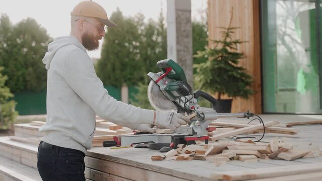 Man cutting wood using table saw on construction site of a modern wooden house. Man working on a house project outside at the sunset. Construction of Scandinavian barnhouse. High quality 4k footage