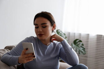Portrait of young brunette woman with concentrated facial expression sitting on the couch typing on the phone. Joyful female having a video call. Background, copy space, close up.