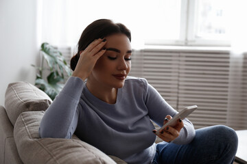 Portrait of young brunette woman with satisfied facial expression sitting on the couch texting and smiling. Joyful female having fun video phone call. Background, copy space, close up.