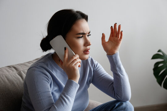 Portrait Of Irritated Young Woman Arguing On Phone. Outraged Female Talking Angrily, Shouting At Cellphone. Customer Support Frustration Concept. Copy Space For Text, White Wall Background, Close Up.