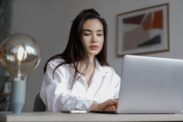 Young beautiful brunette woman at the office, copywriter typing a new text on her laptop. Portrait...