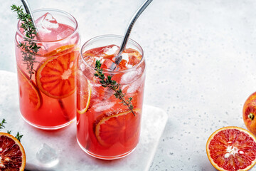 Blood Orange lemonade cocktail with ice and thyme on light gray concrete background