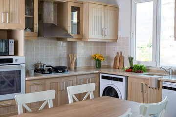 Kitchen with classic style interior. Wooden furniture, gas cooktop and separate electric wall oven, wooden utensil, fresh fruits and vegetables on marble tabletop. Copy space, background, close up.