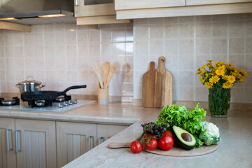 Close up shot of different raw fruits, vegetables and greens, wooden chopping boards on the marble countertop of kitchen with classic style interior. Pastel color facing tiles. Copy space, background.
