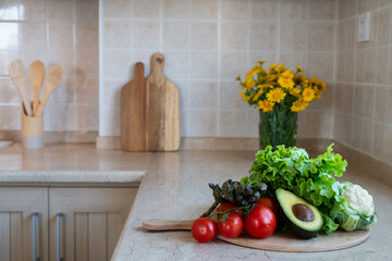 Close up shot of different raw fruits, vegetables and greens, wooden chopping boards on the marble countertop of kitchen with classic style interior. Pastel color facing tiles. Copy space, background.