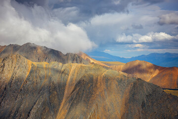 Colorful landscape of mountain peaks. Ridge of rocks under majestic cloudy sky, view from top. Altai, Siberia.